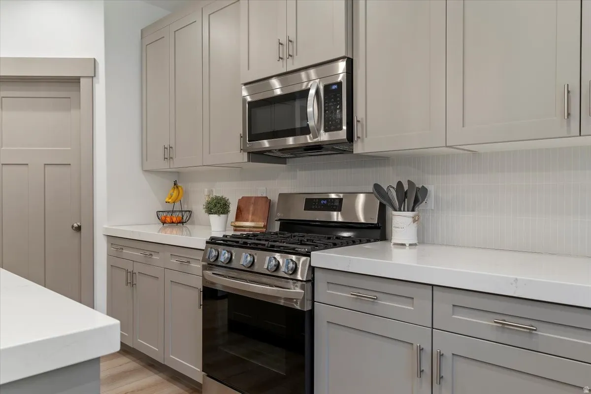 Contemporary kitchen featuring grey shaker-style cabinetry, stainless steel appliances including a range and over-the-range microwave, white countertops, and a white tile backsplash