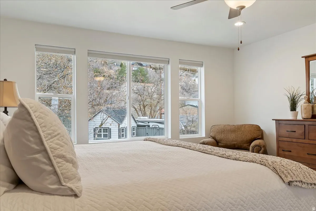 Bedroom featuring a wall of windows, overhead ceiling fan with lighting, white walls, and wood-finish dresser with an integrated mirror
