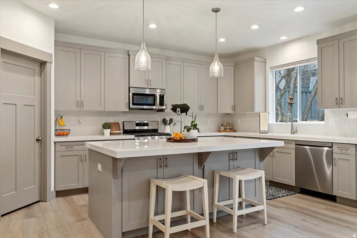 Contemporary kitchen featuring light gray cabinetry, stainless steel appliances, a center island with seating, pendant lighting, and wood-finish flooring