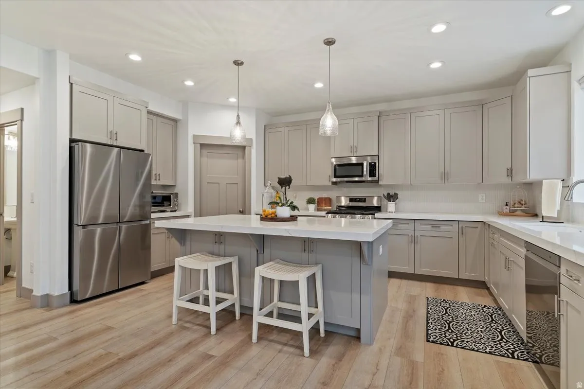 Contemporary kitchen featuring a spacious island with seating, stainless steel appliances, light gray cabinetry, light countertops, and wood-finish flooring