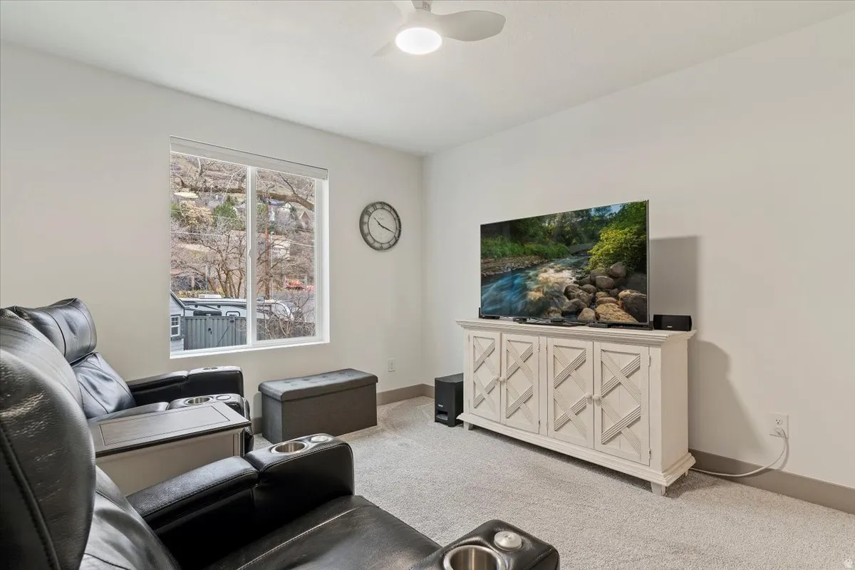Carpeted interior space featuring a large window, white walls, and a ceiling fan