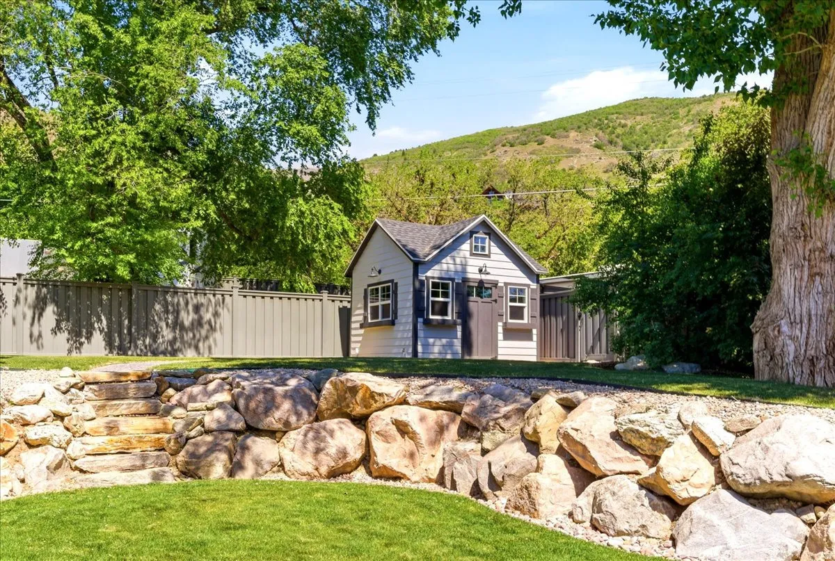 Landscaped backyard featuring a tiered rock retaining wall with stone steps, a manicured lawn, and a custom storage shed with board and batten siding