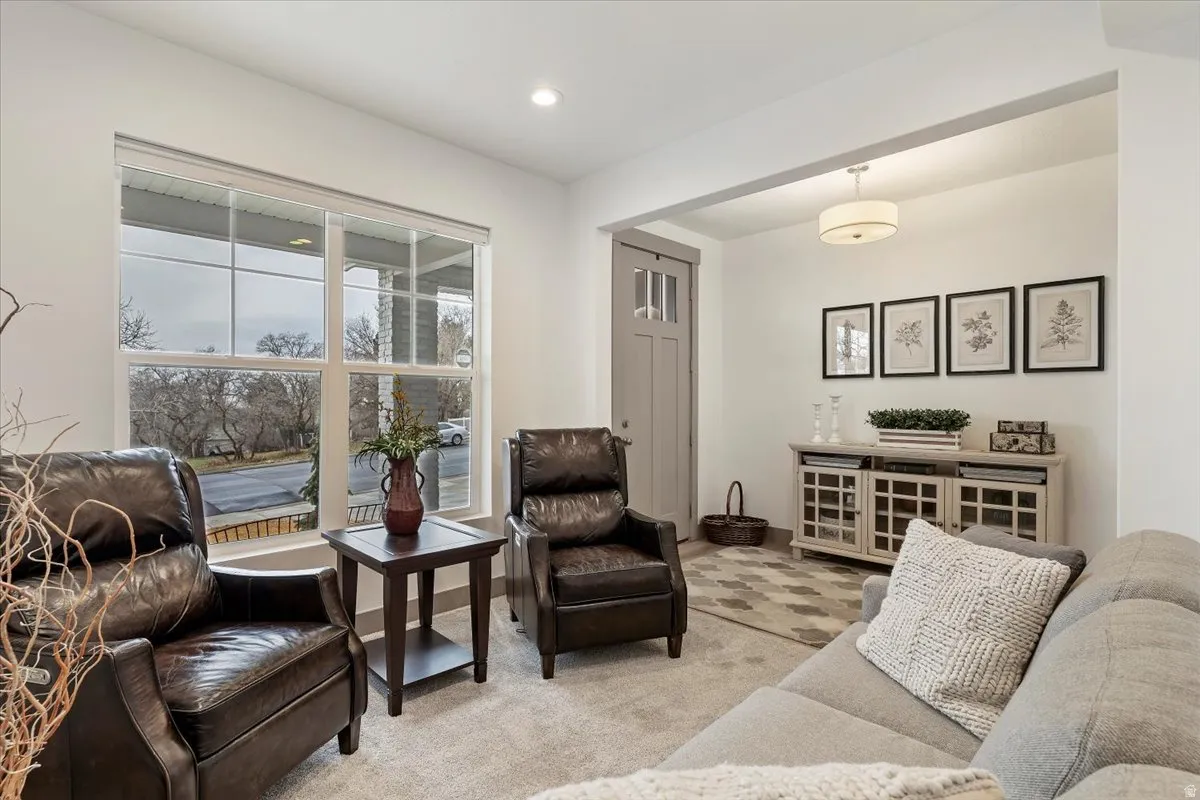 Bright living area featuring a large window with white trim, soft gray carpeting, a neutral wall color, a light wood-finish console cabinet, and a contemporary flush-mount ceiling light