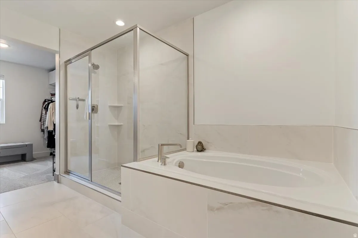 Spacious bathroom featuring a built-in soaking tub with deck-mounted fixtures, a glass-enclosed shower with tile surround and recessed shelving, and large format tile flooring