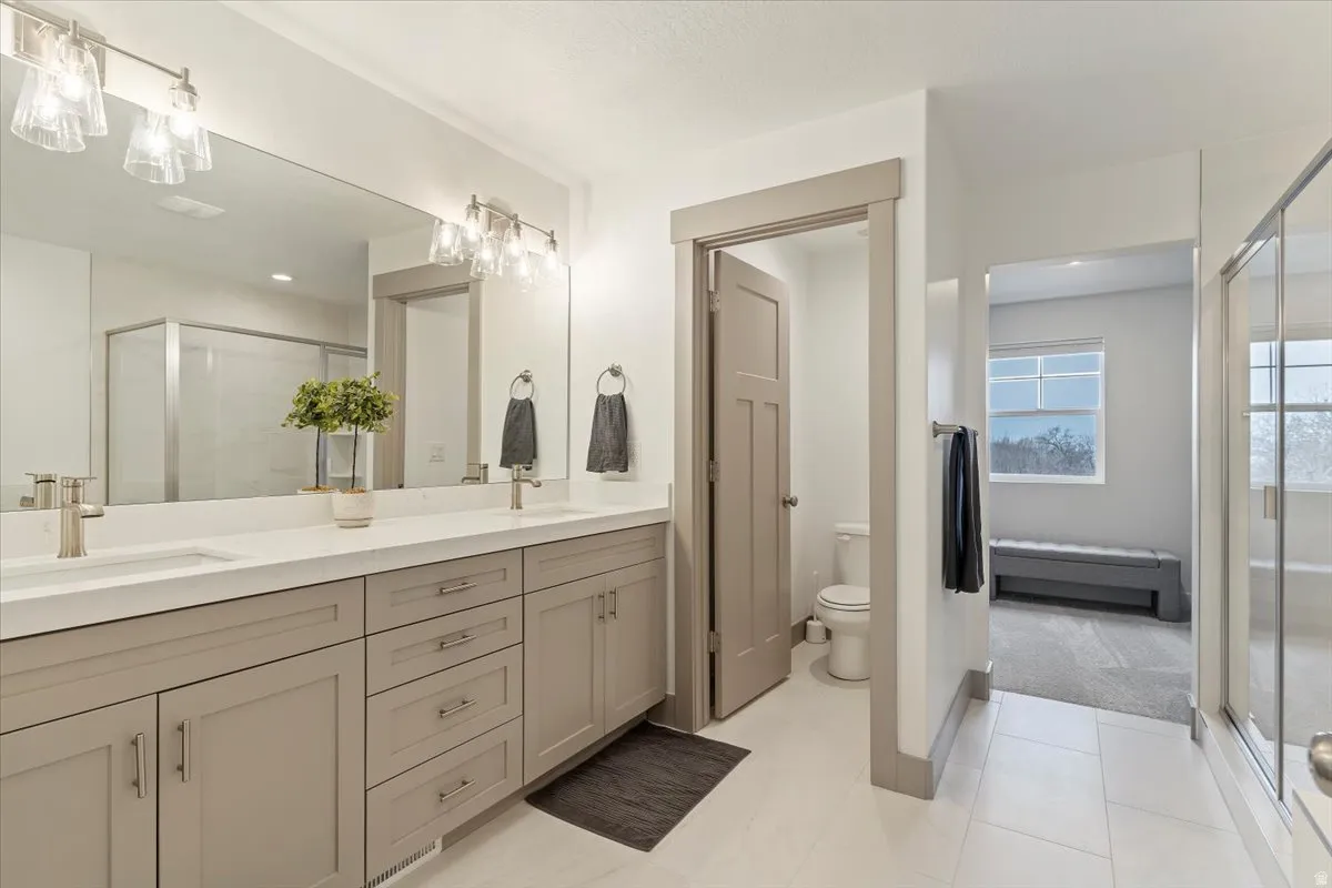 Spacious bathroom featuring a dual vanity with light-toned cabinetry and brushed nickel hardware, expansive mirror, and a glass-enclosed shower