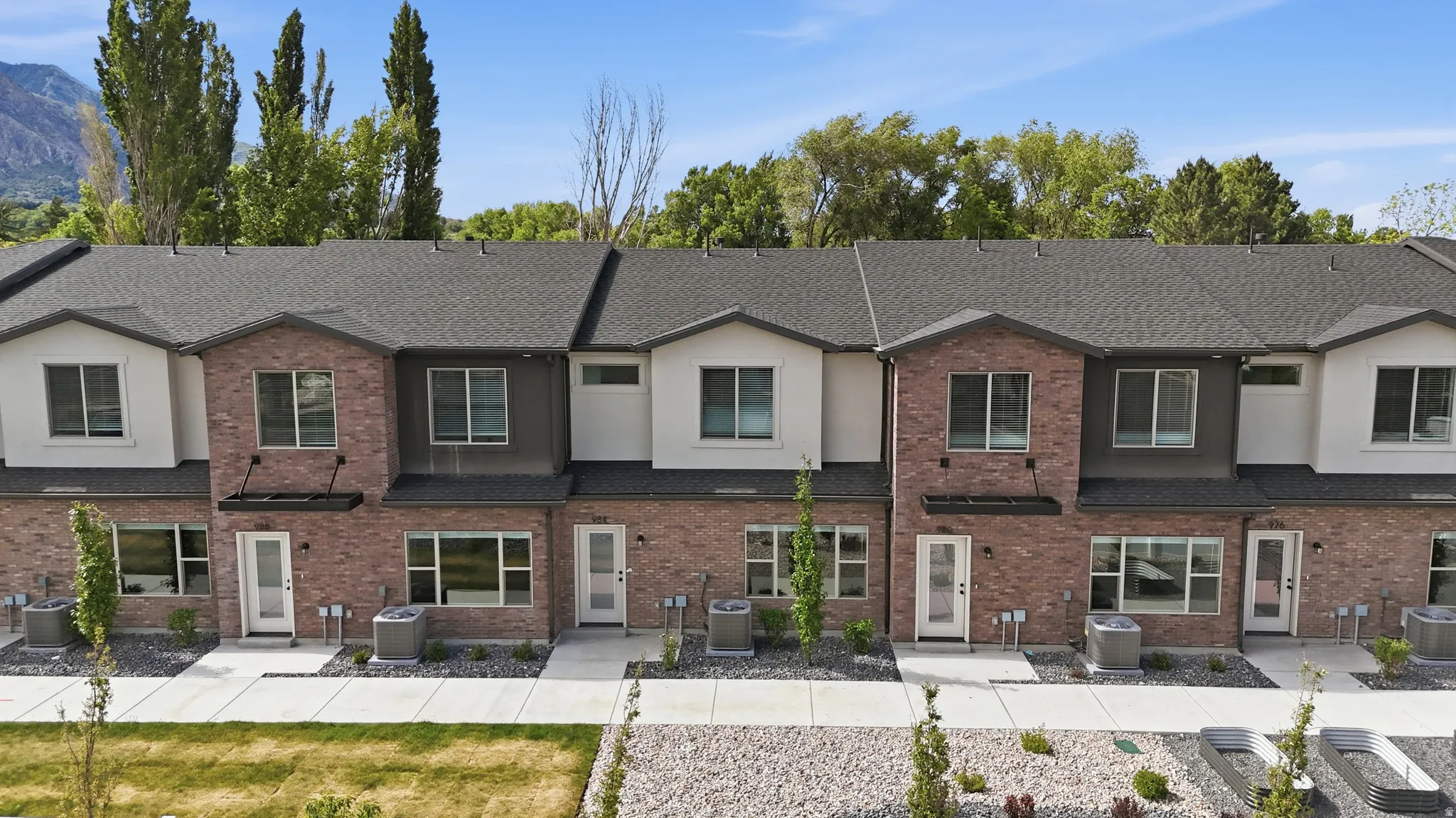 Contemporary townhome row featuring brick and stucco facades, dark shingle roofing, and individual front entrances