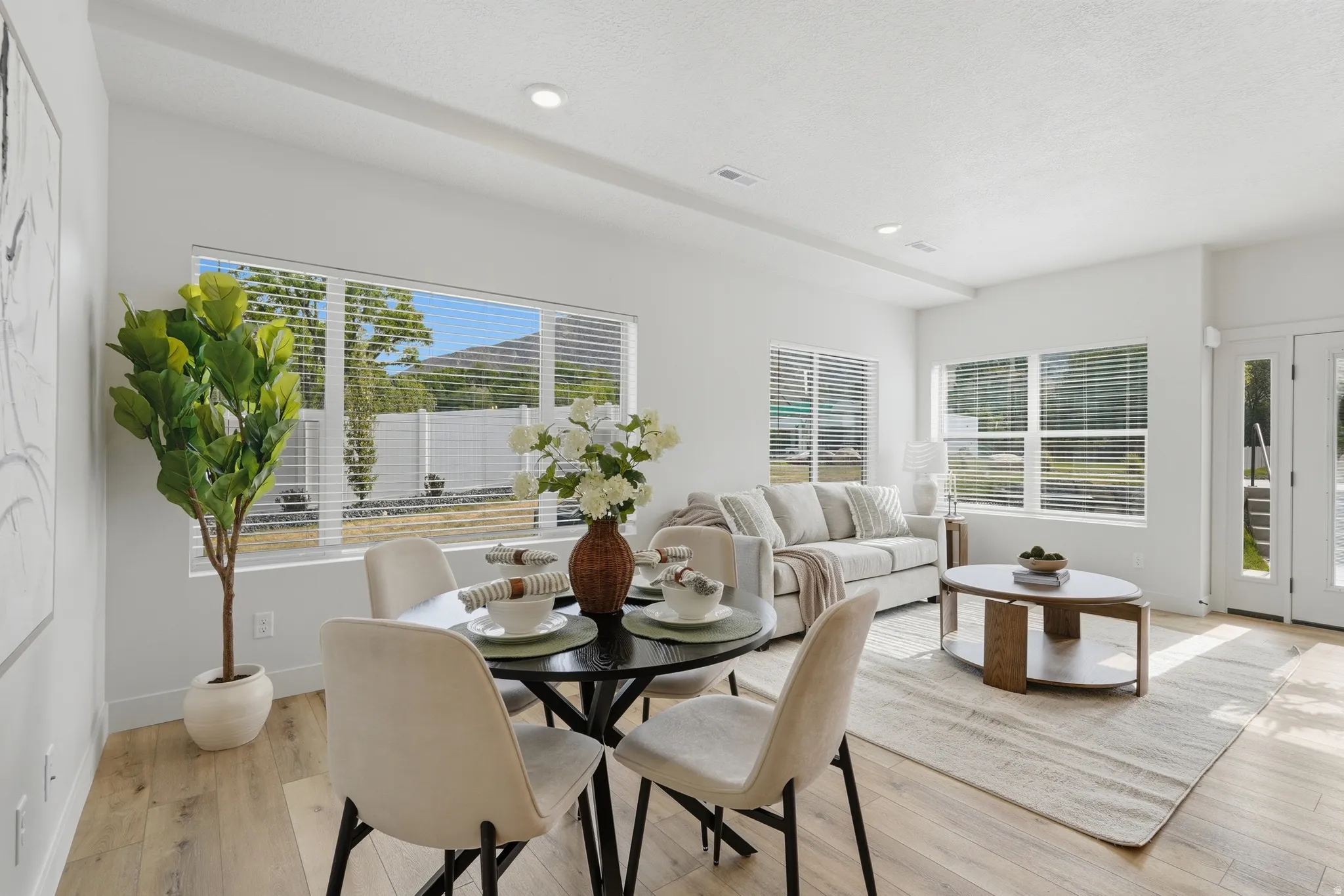 Open-concept living area featuring wood-finish flooring, recessed lighting, and expansive windows with horizontal blinds