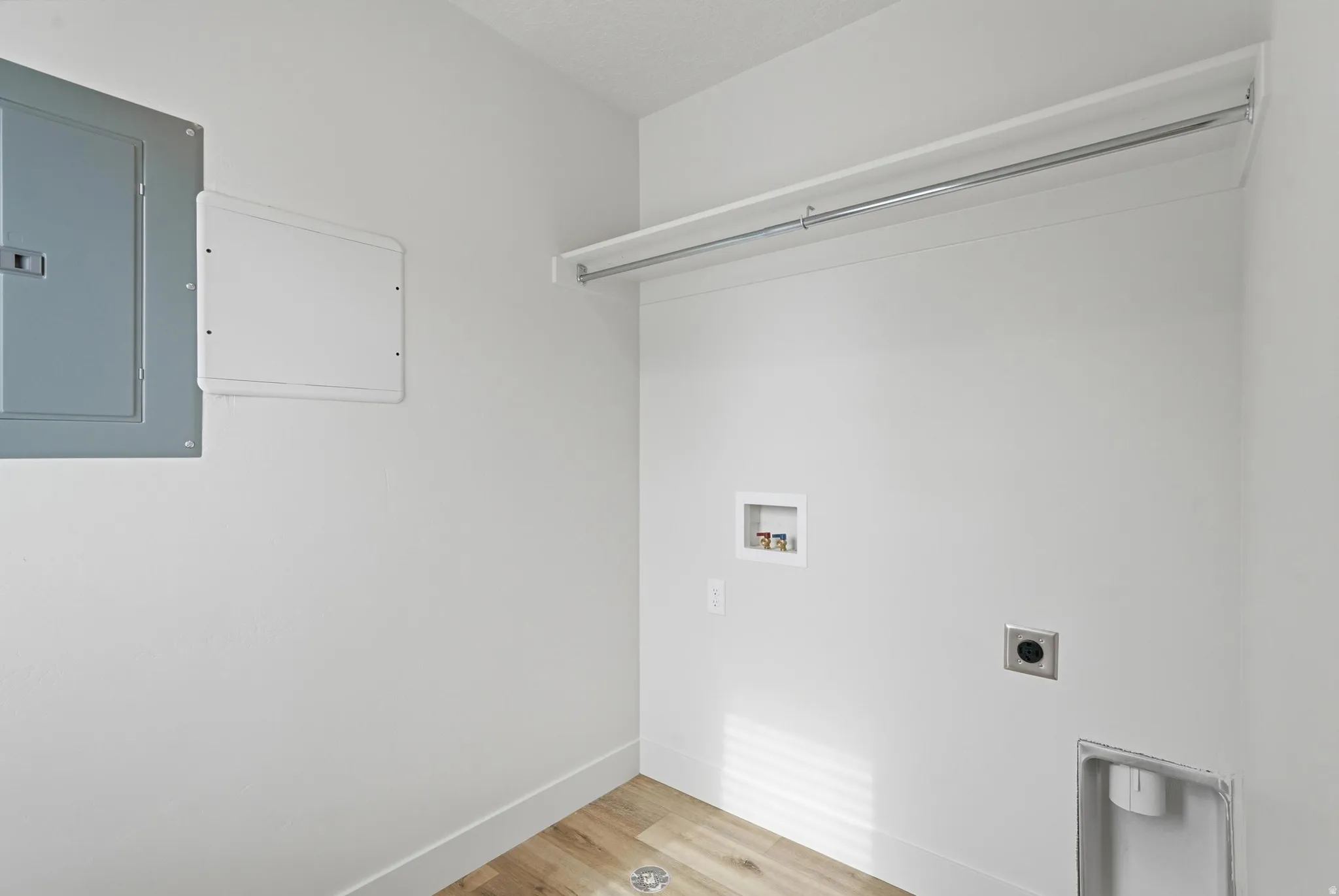 Dedicated laundry area featuring light wood-finish flooring, white baseboards, and bright white walls