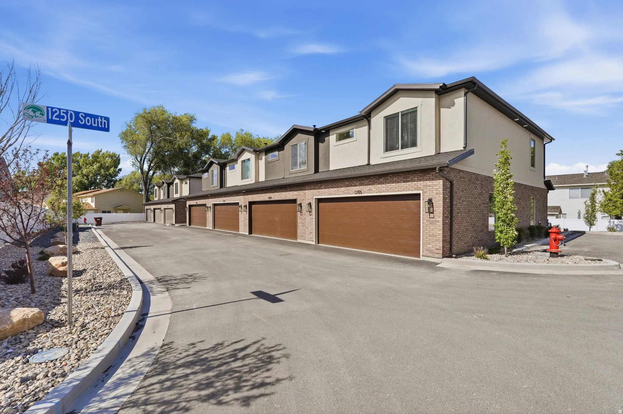 Contemporary townhomes featuring brick and stucco exteriors, individual garages with wood-look doors, and asphalt driveways