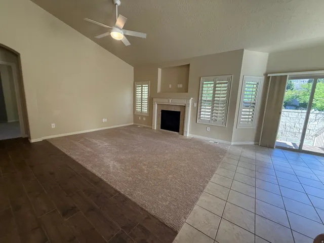 Vaulted ceiling with a ceiling fan, fireplace with a mantel, plantation shutters, sliding glass door, and wood-finish flooring