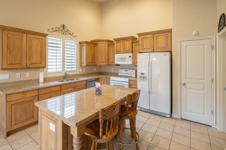 Kitchen featuring wood cabinetry, light-toned countertops, a central island, tile flooring, and white appliances