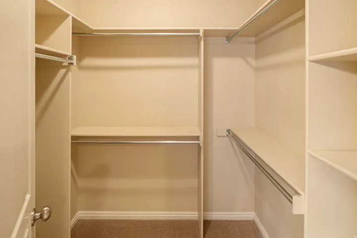 Walk-in closet featuring multiple shelving units, chrome hanging rods, neutral wall color, base molding, and carpet flooring