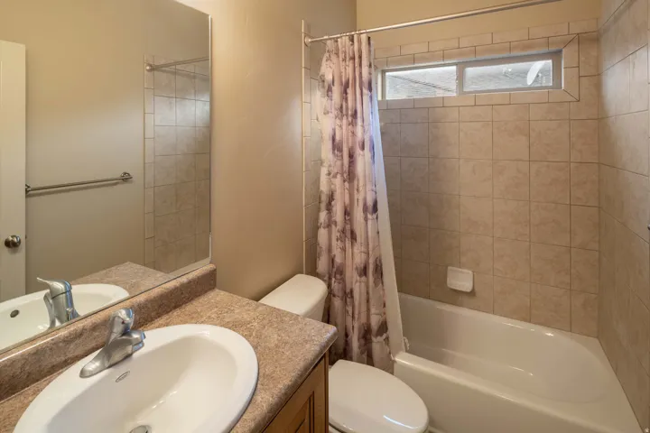 Bathroom featuring a vanity with a laminate countertop and integrated sink, a large wall mirror, and a bathtub with tile surround