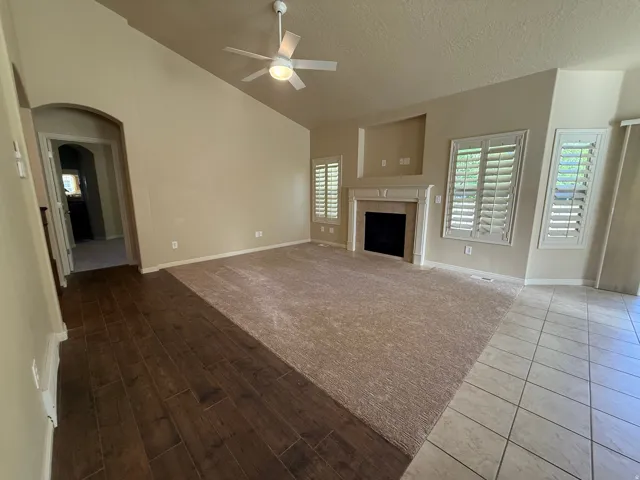 Vaulted ceiling, ceiling fan, fireplace with mantel, window shutters, and mixed flooring