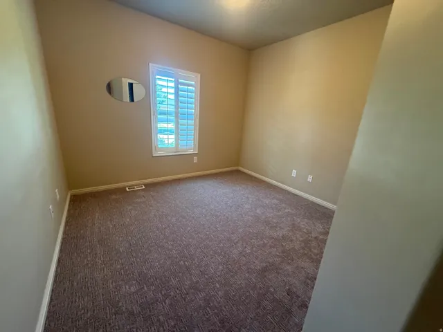 Textured carpeting, neutral wall finishes, window with plantation shutters, and a ceiling-mounted light fixture
