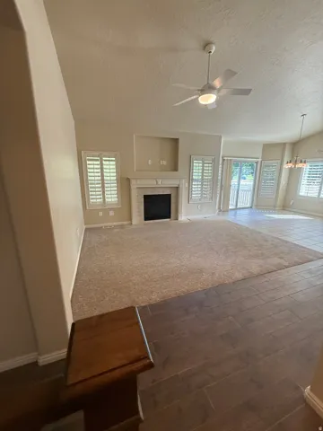 Spacious open living area featuring high ceilings with ceiling fan, fireplace with surround, multiple sets of plantation shutters, and wood-finish flooring throughout select zones