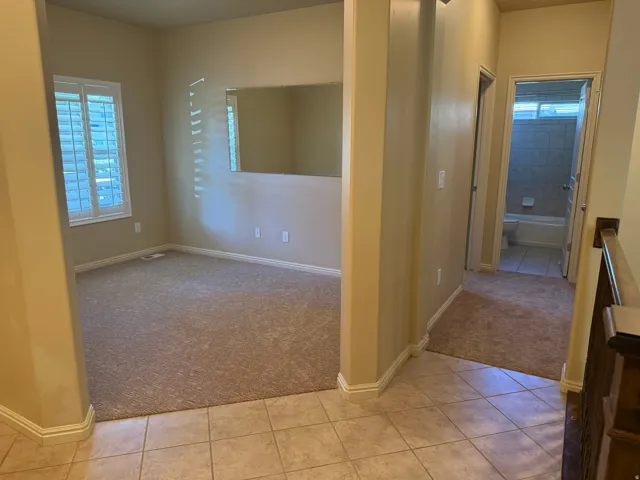 Neutral color palette, tile flooring, carpeted room, window with plantation shutters, hallway access