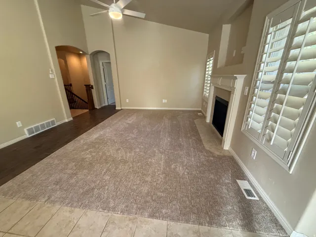 Vaulted ceiling with a ceiling fan, fireplace with a mantel, window shutters, and mixed flooring featuring carpet, wood-finish, and tile
