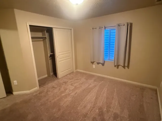 Wall-to-wall carpeting with light beige walls, double-door closet with internal shelving, and a single window with blinds