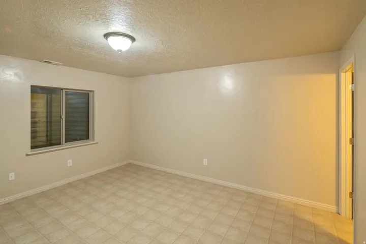 Spacious room featuring neutral wall tones, tile flooring, a horizontal sliding window, a flush mount ceiling light fixture, and white baseboards