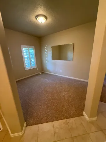 Carpeted room with a flush-mount ceiling light and a window featuring white plantation shutters