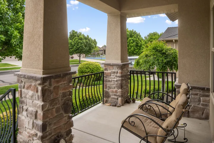 Covered front porch featuring textured stucco pillars with stone bases, wrought iron railings, and a concrete surface