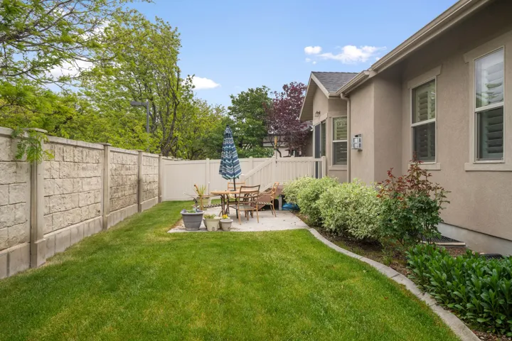 Expansive backyard featuring a manicured lawn, a concrete block privacy wall, and a white vinyl fence