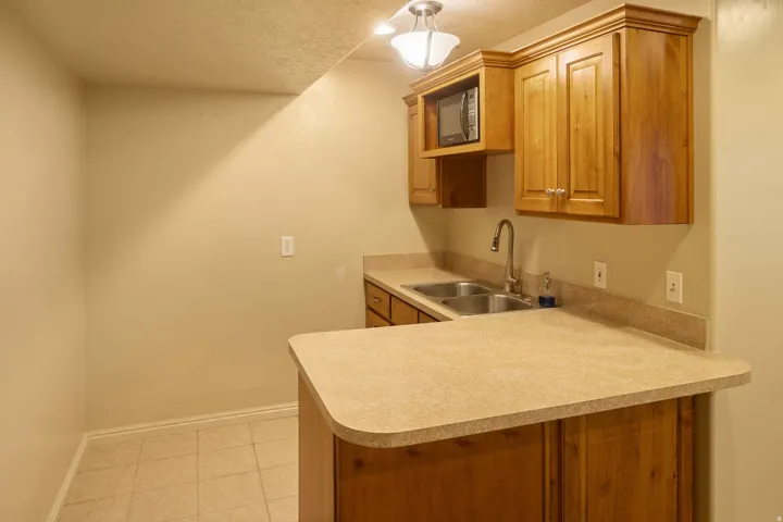 Functional kitchenette featuring wood cabinetry, a built-in microwave, a double basin stainless steel sink, and light-toned countertops