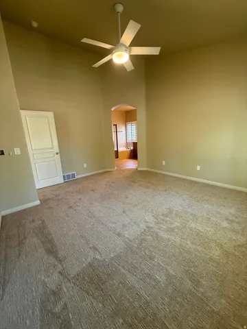 Vaulted ceiling with a ceiling fan, carpeted flooring, and an arched doorway
