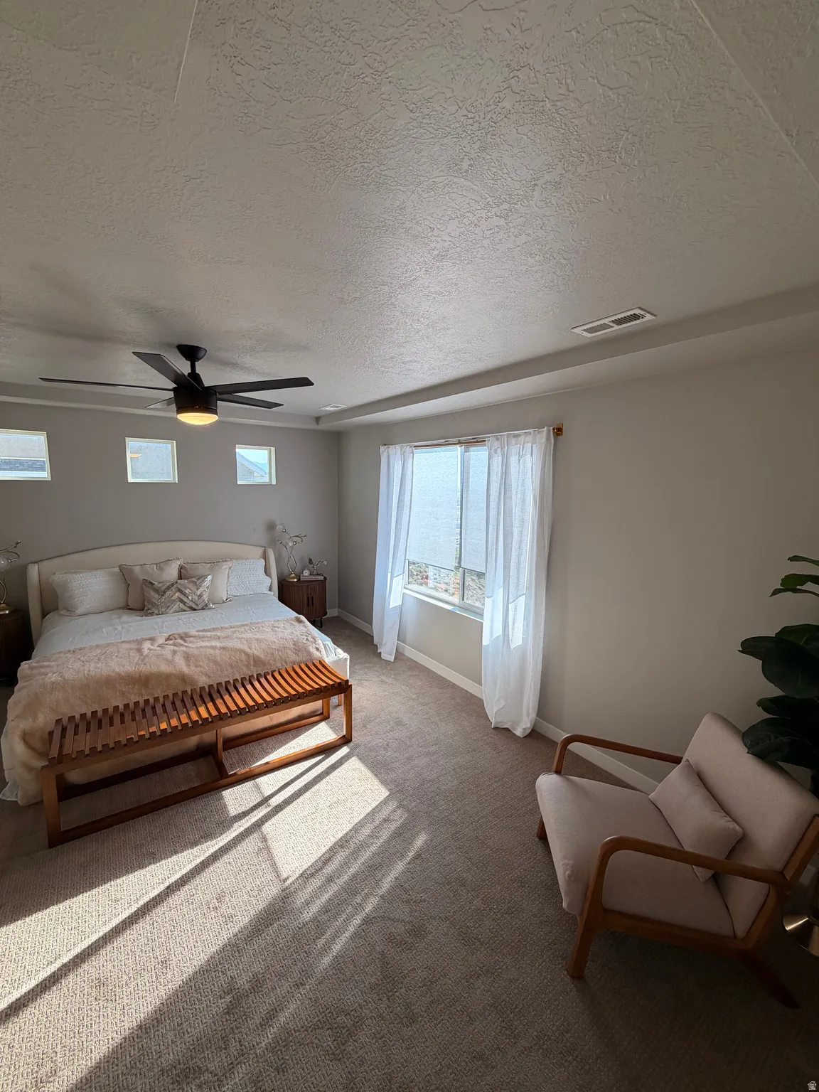 Carpeted room featuring a recessed ceiling, ceiling fan with integrated lighting, and multiple windows with drapery