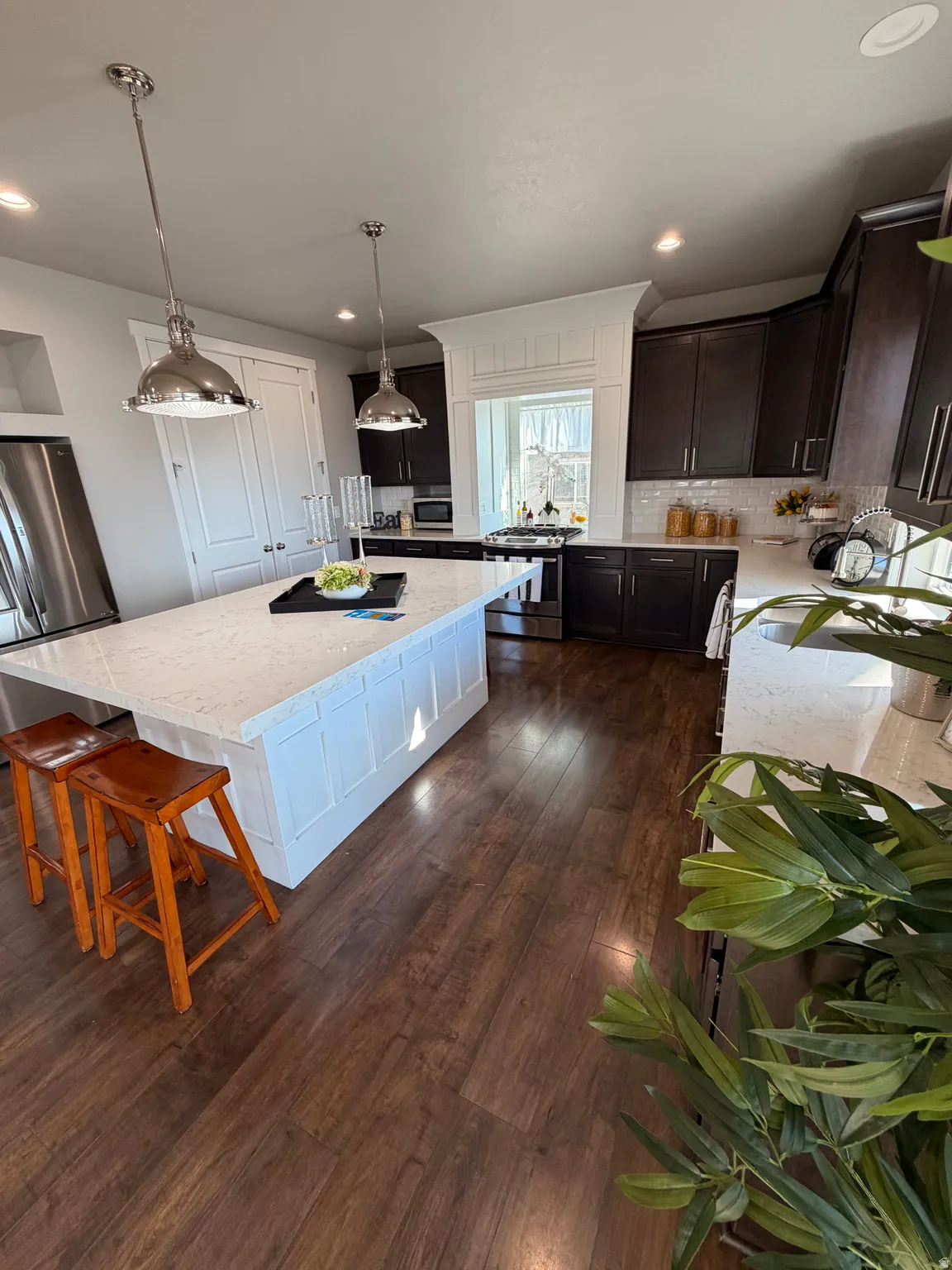 Open-concept kitchen featuring an oversized island with white paneled cabinetry, light-toned countertops, and two polished pendant lights