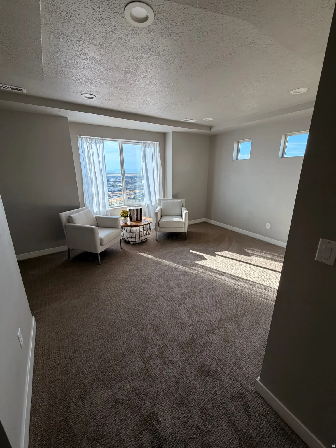 Spacious room featuring broadloom carpet, recessed lighting, a large picture window with white drapery, and additional rectangular windows providing natural light