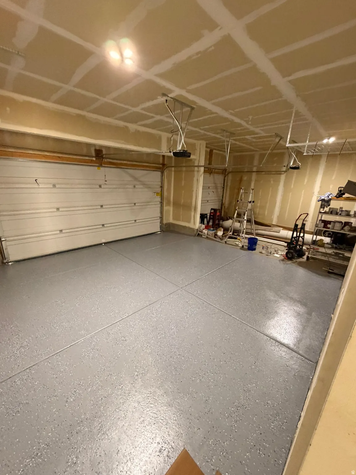 Spacious garage featuring a durable epoxy-coated floor, two overhead garage doors, and multiple ceiling-mounted light fixtures