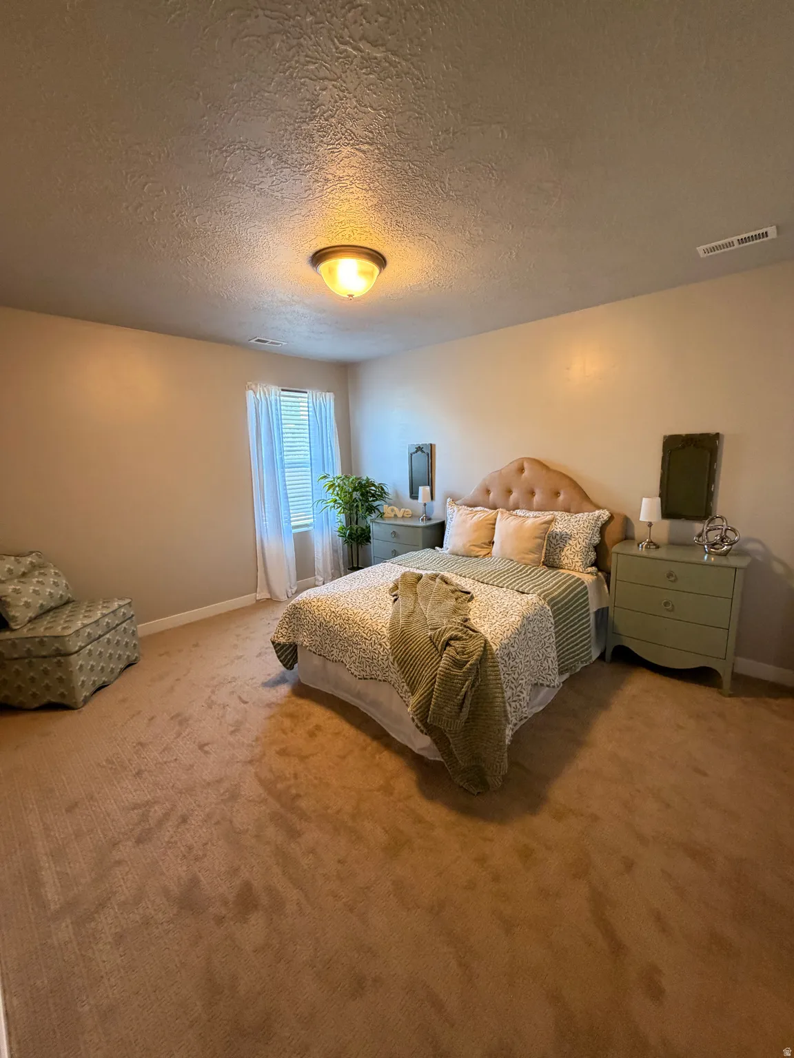 Carpeted room featuring a window with white drapes, a textured ceiling, and a flush mount light fixture