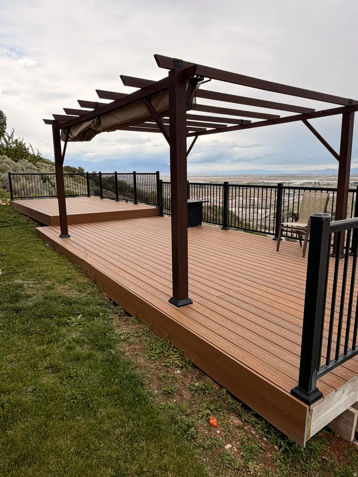 Expansive multi-level wood-finish deck featuring a dark brown pergola with a retractable canopy