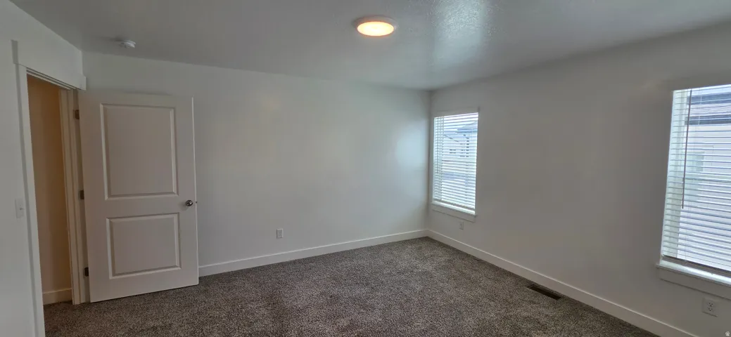 Carpeted room featuring white walls, a white two-panel interior door, and two windows with blinds