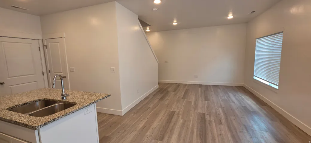 Kitchen island with a double basin stainless steel sink and granite-style countertop, wood-finish flooring, recessed lighting, and a white interior paint scheme