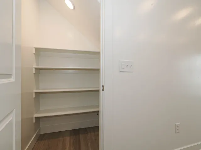 Under-staircase storage featuring multiple built-in shelves, wood-finish flooring, recessed lighting, and a neutral color palette