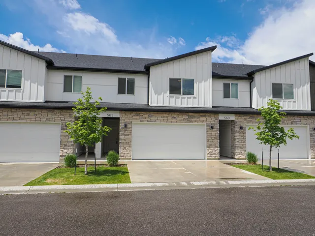 Contemporary townhome exterior featuring white vertical siding, dark architectural shingles, stone veneer accents, and an attached garage with a concrete driveway