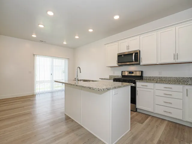 Kitchen featuring an island with a stainless steel sink and faucet, granite countertops, white cabinetry with brushed nickel hardware, and stainless steel appliances