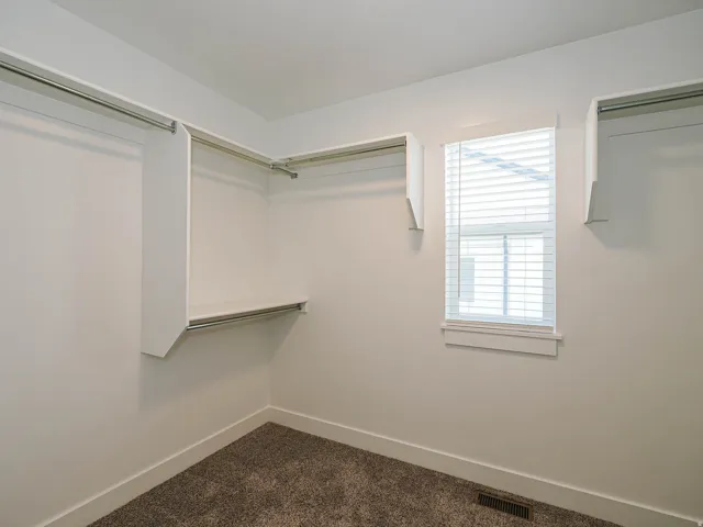 Walk-in closet featuring white built-in shelving, chrome hanging rods, and a window with blinds