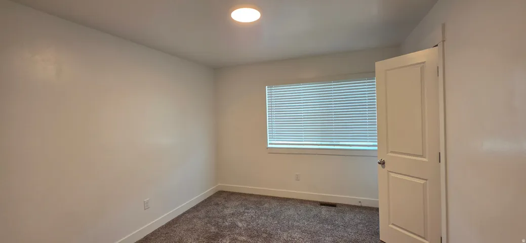 Neutral wall paint with textured carpeting, a window featuring horizontal blinds, and a flush-mount ceiling light fixture