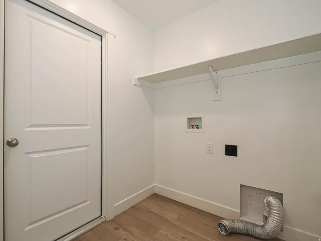 Dedicated utility space featuring wood-finish flooring, a white paneled door, a wall-mounted white shelf, and essential appliance hookups