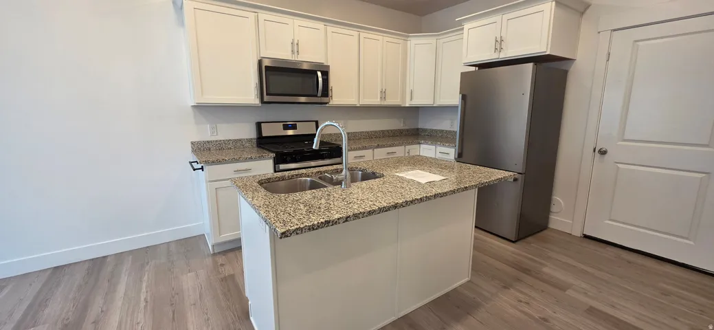 Kitchen featuring a central island with double basin sink, granite countertops, white cabinetry, and stainless steel appliances