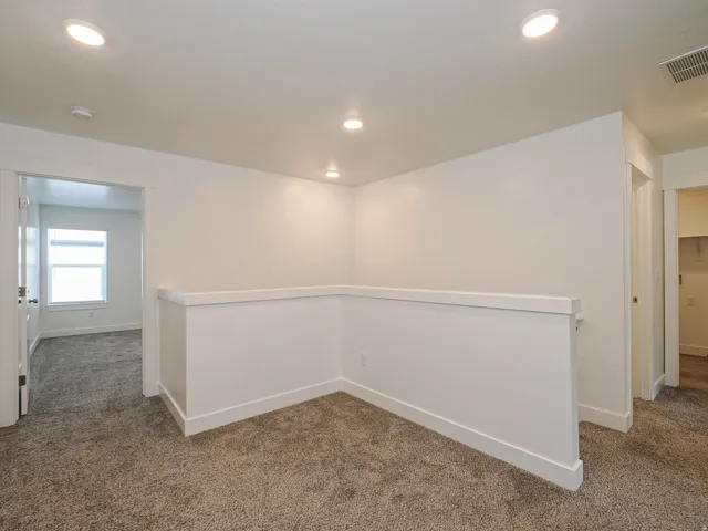 Carpeted loft area featuring recessed lighting, a white half-wall railing, and doorways providing access to additional rooms