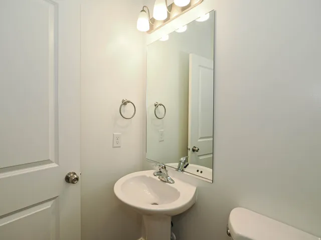 Pedestal sink with chrome faucet, wall-mounted mirror, and vanity lighting