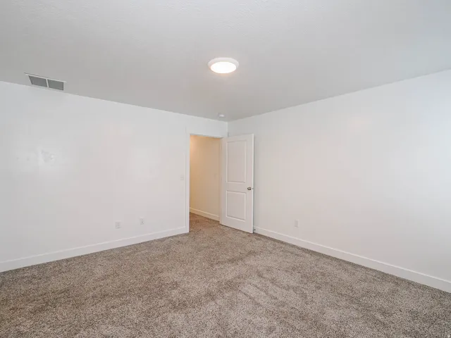 Neutral tone wall finishes, gray carpet flooring, white baseboards, and a white interior door with a silver knob