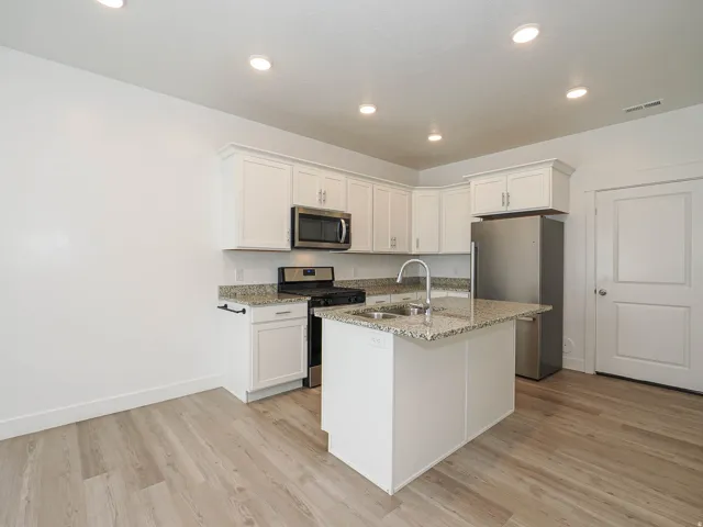 Kitchen featuring white cabinetry, granite countertops, stainless steel appliances, a central island with an undermount sink, and wood-finish flooring