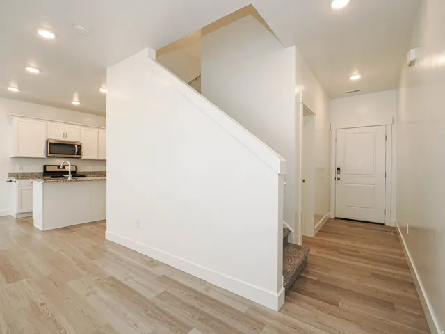 Open-concept living space featuring wood-finish flooring, recessed lighting, and a modern kitchen with white cabinetry, stainless steel appliances, and granite countertops