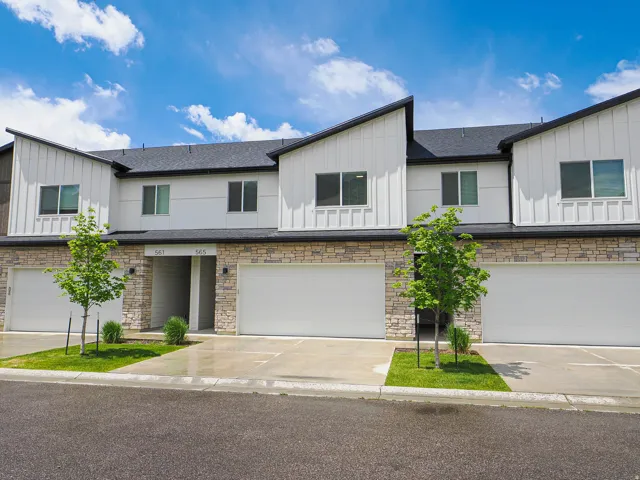 Modern townhome exterior featuring light-colored vertical siding, stone accents, dark-framed windows, and multiple attached garages